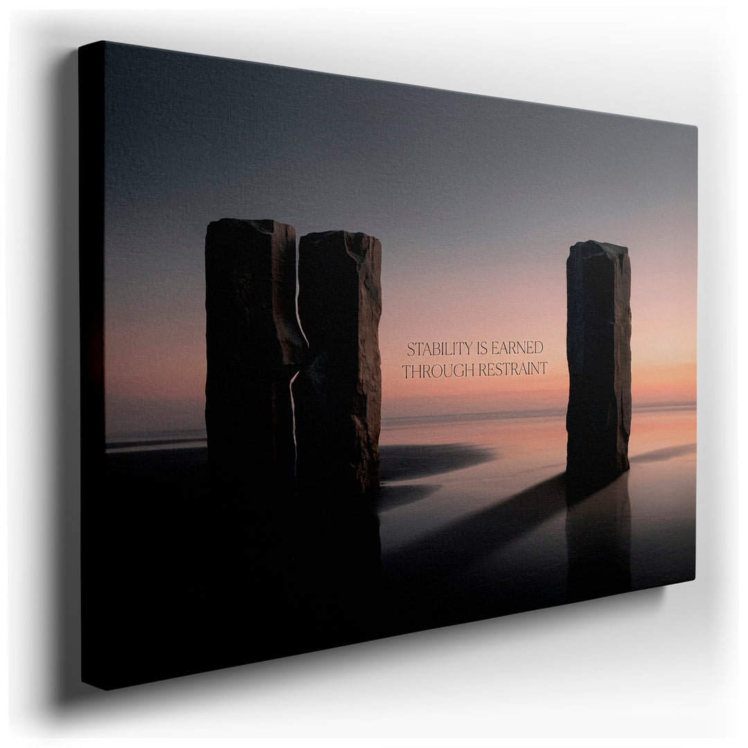 Abstract wall art showing stone pillars on a beach at sunrise, expressing 'Stability is Earned Through Restraint'.