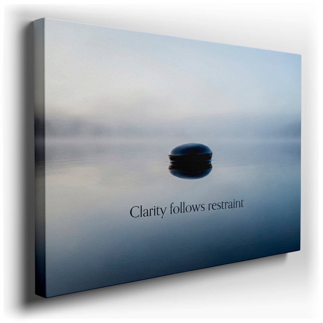 A smooth, dark stone rests on a misty lake with the text 'Clarity follows restraint'. Serene wall art.
