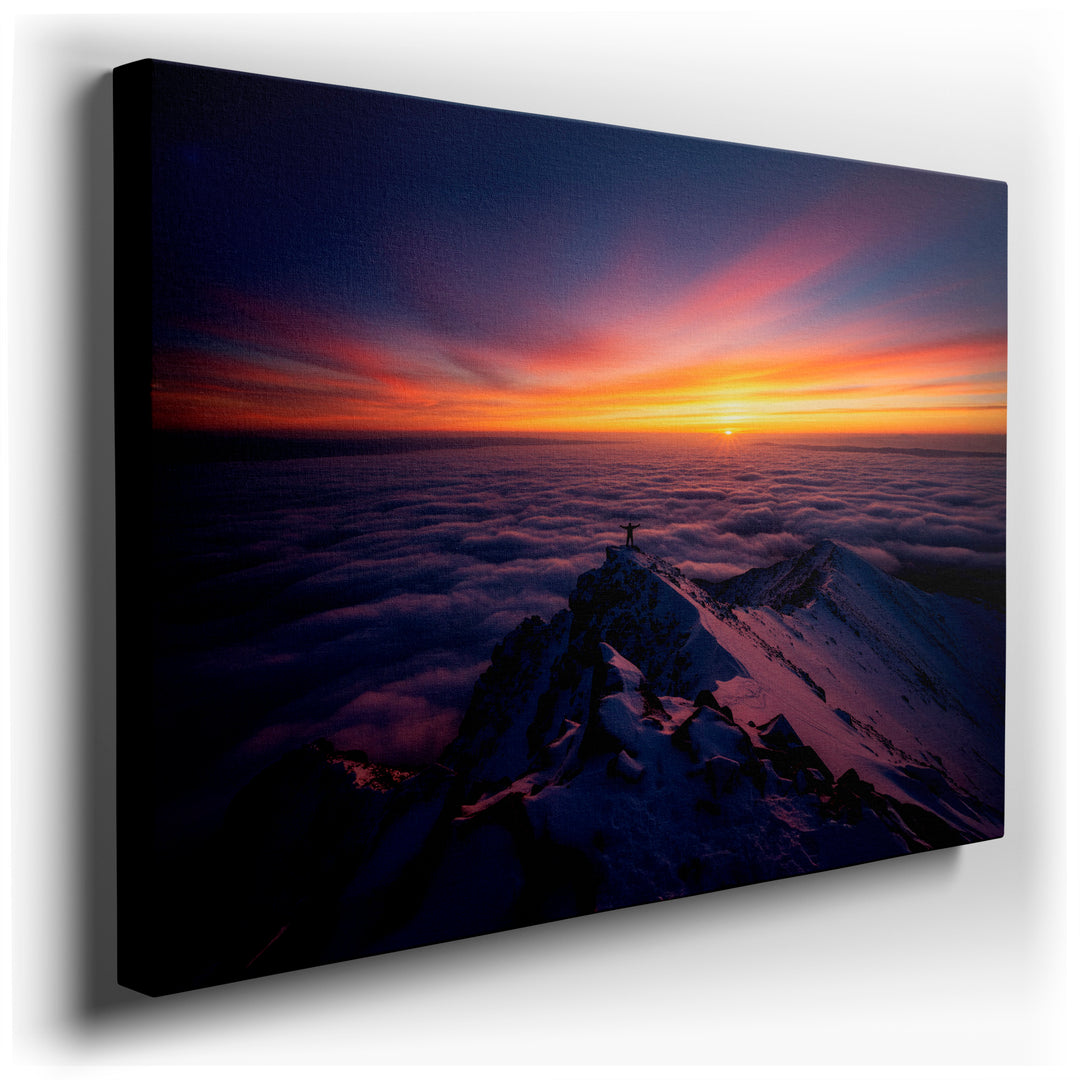 A person stands atop a snowy mountain, silhouetted against a sunrise over a sea of clouds. Stunning wall art.
