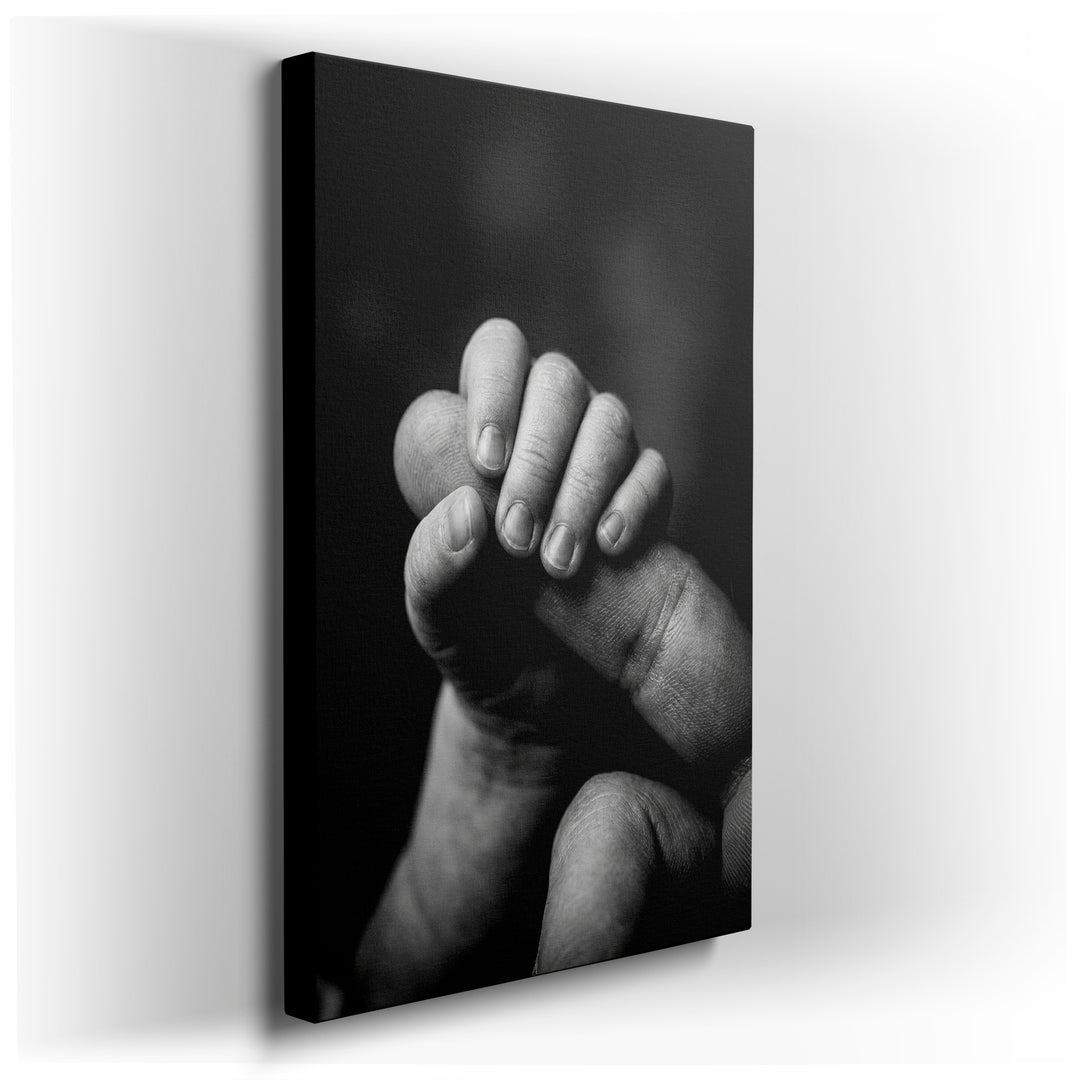 A touching black and white image shows a baby's tiny hand gently clasping an adult's finger. Sentimental wall art.